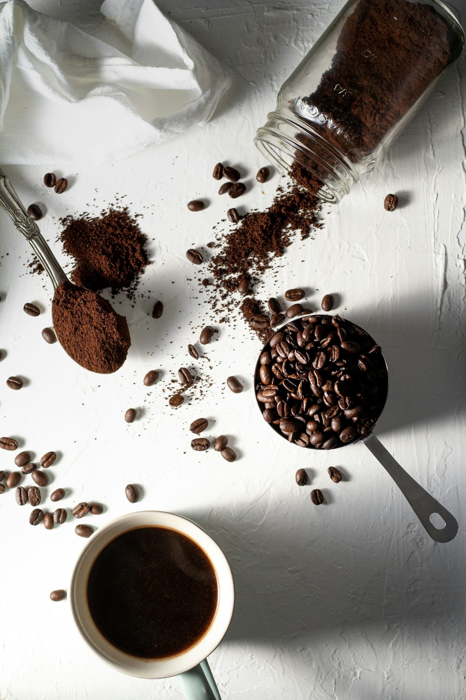 Coffee beans, ground coffee and a fresh cup on a white table