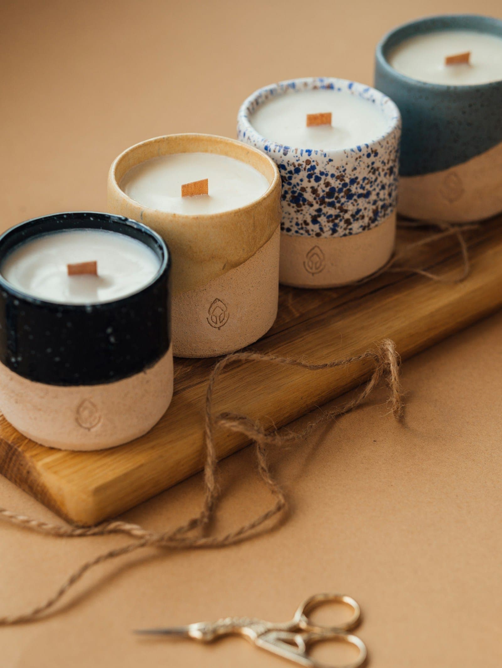 Four wood-wick candles in speckled ceramic vessels