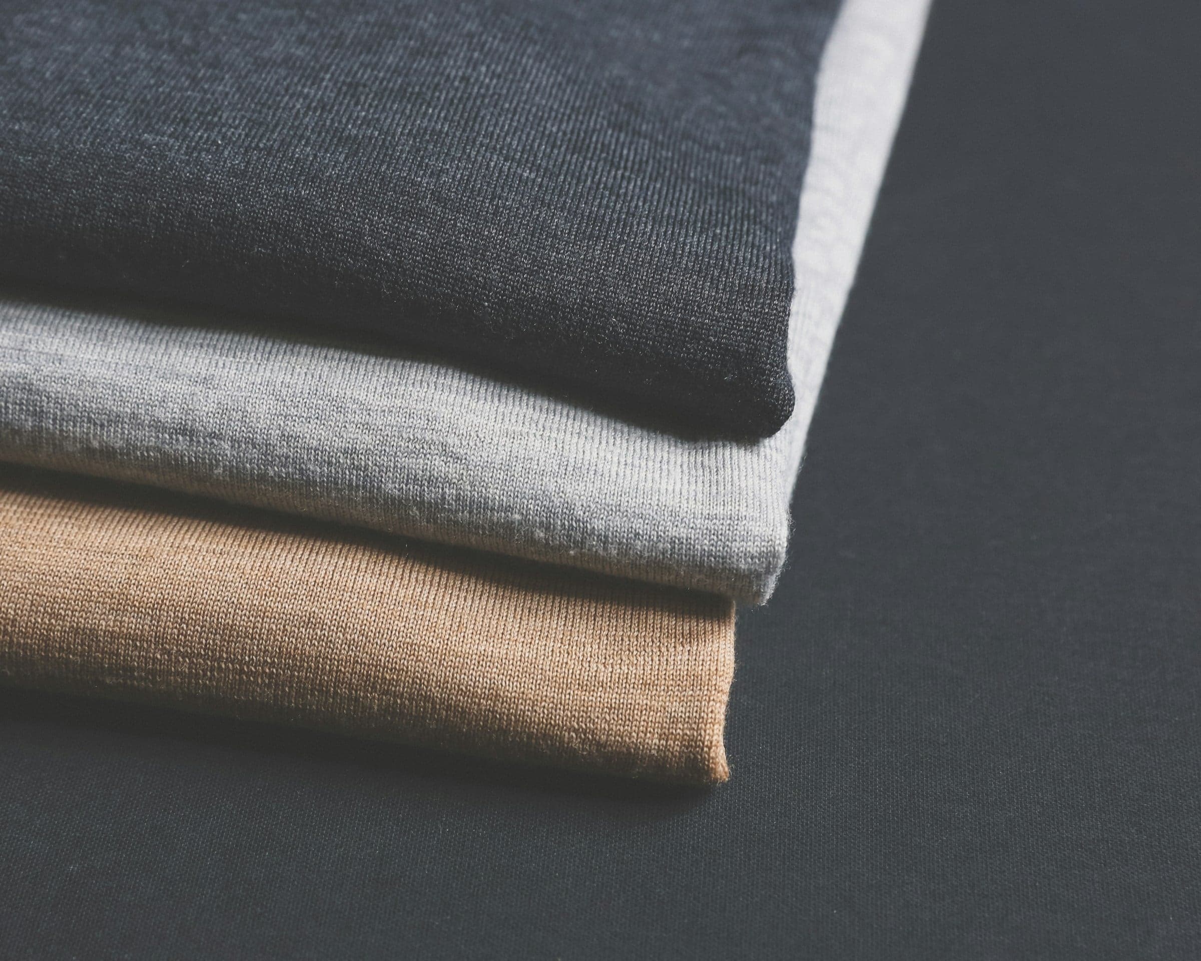 A stack of folded knitwear in grey, charcoal and camel