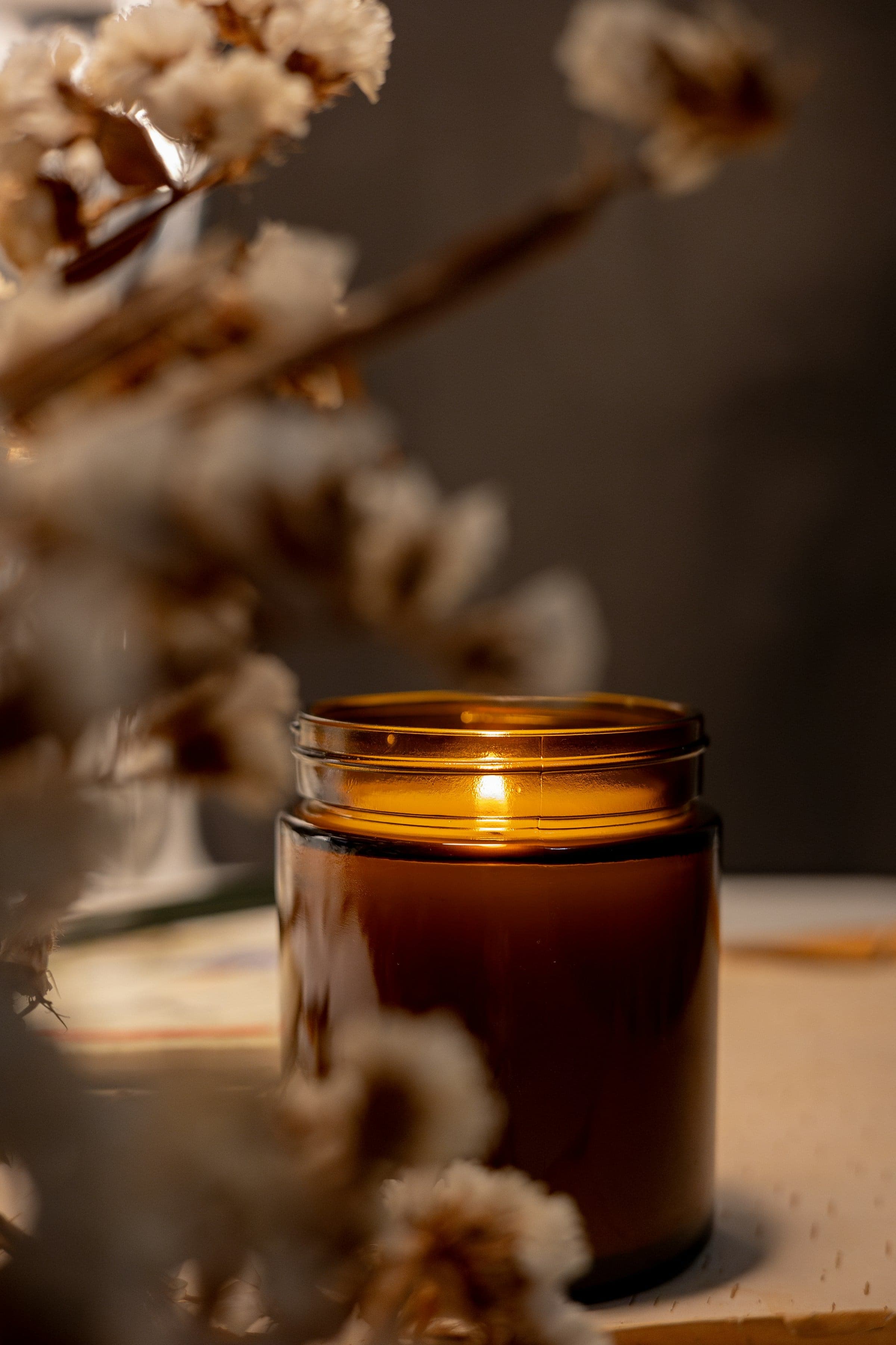 A lit candle in an amber glass jar beside dried flowers