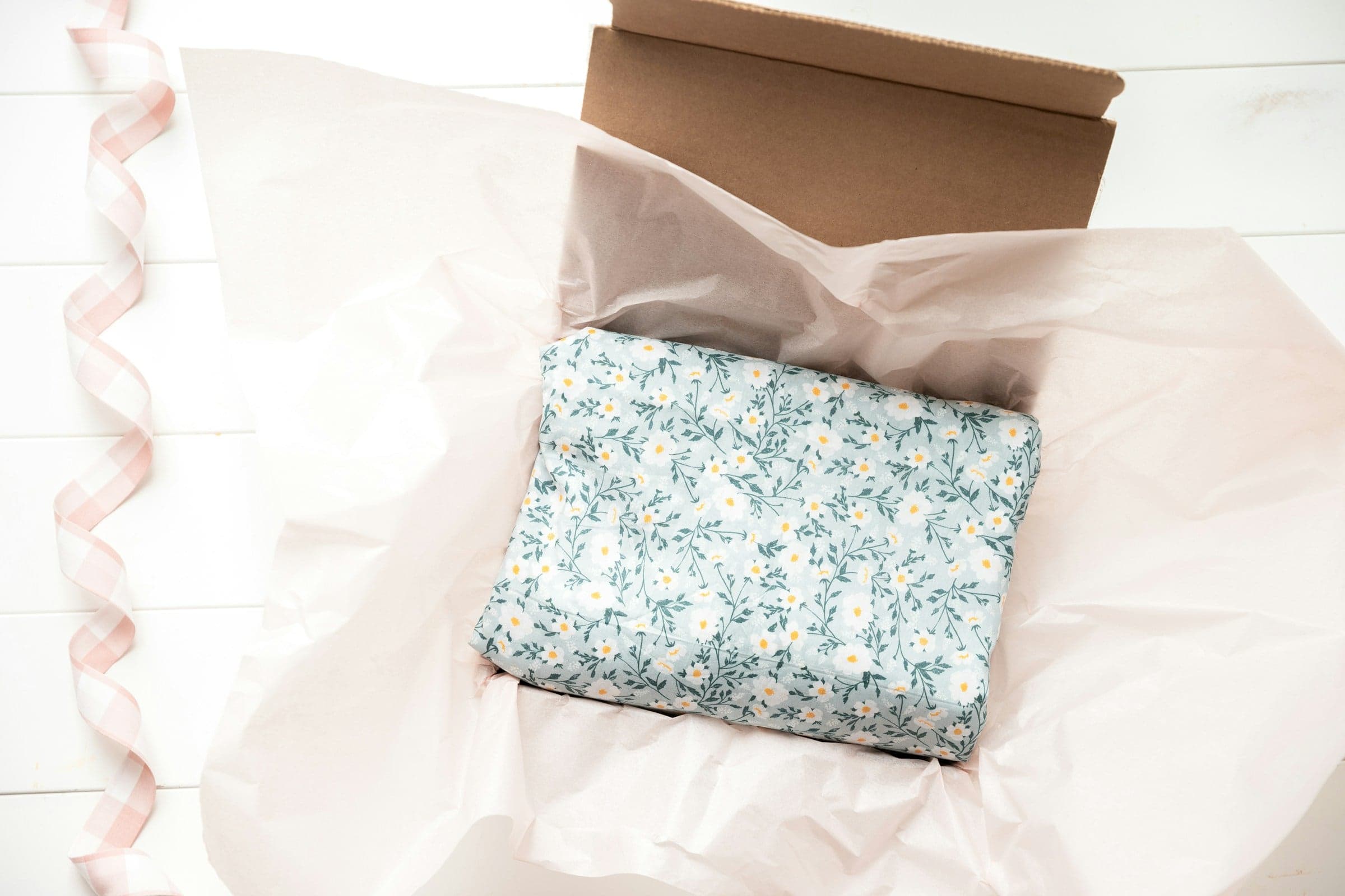 A gift box lined with tissue paper, holding a folded floral cloth