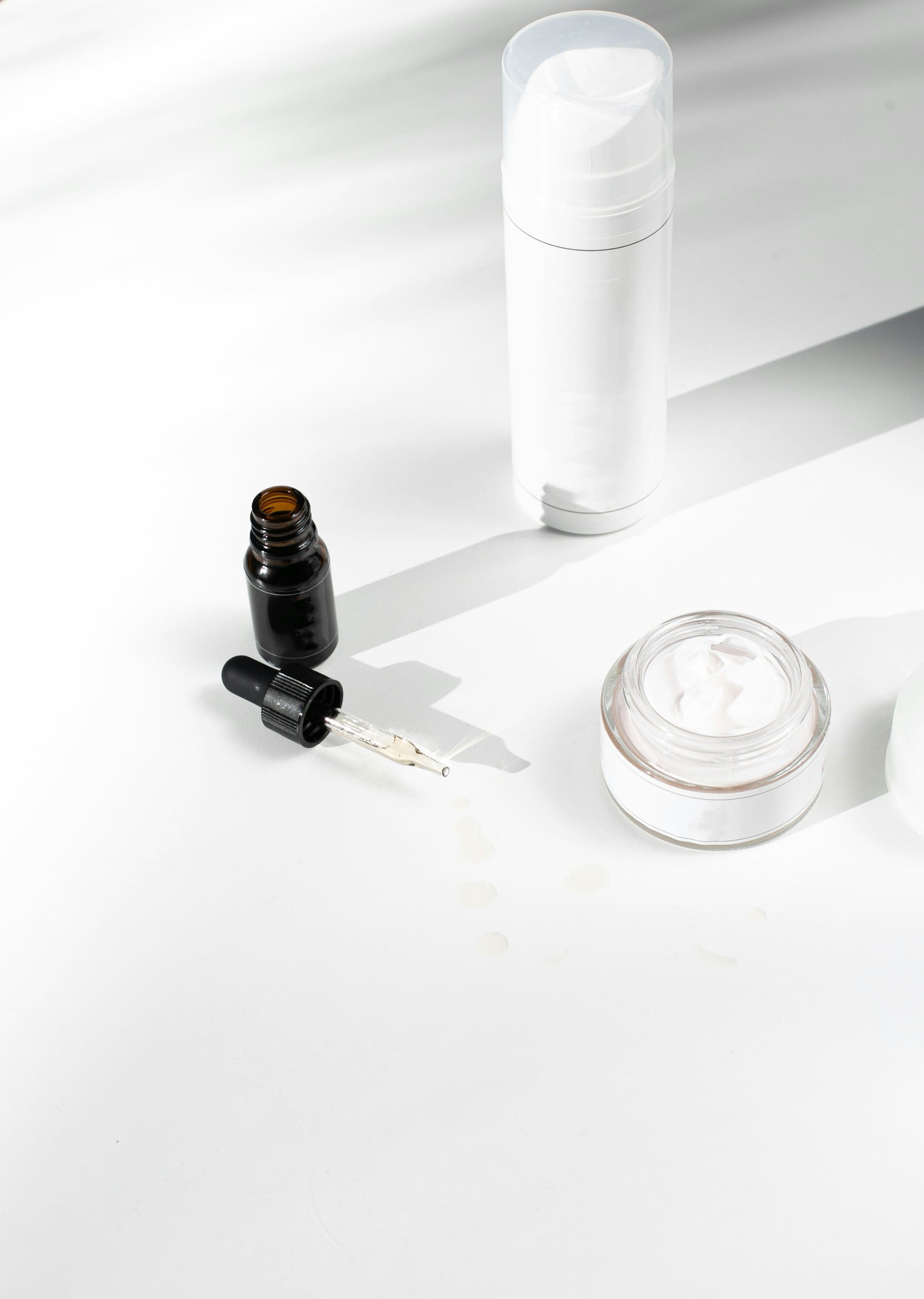 A serum, a dropper bottle and a jar of cream in soft light